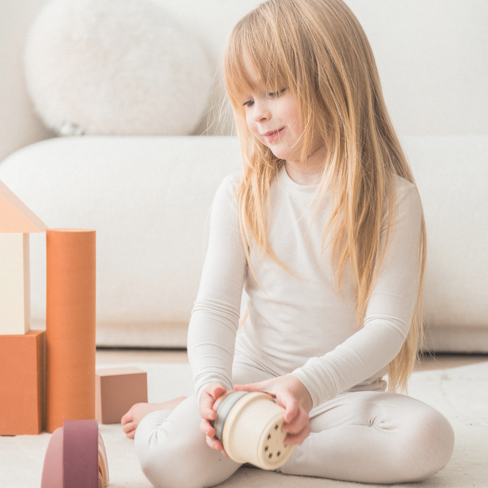 A girl playing with blocks on the floor in her neutral Milana Label pj set.