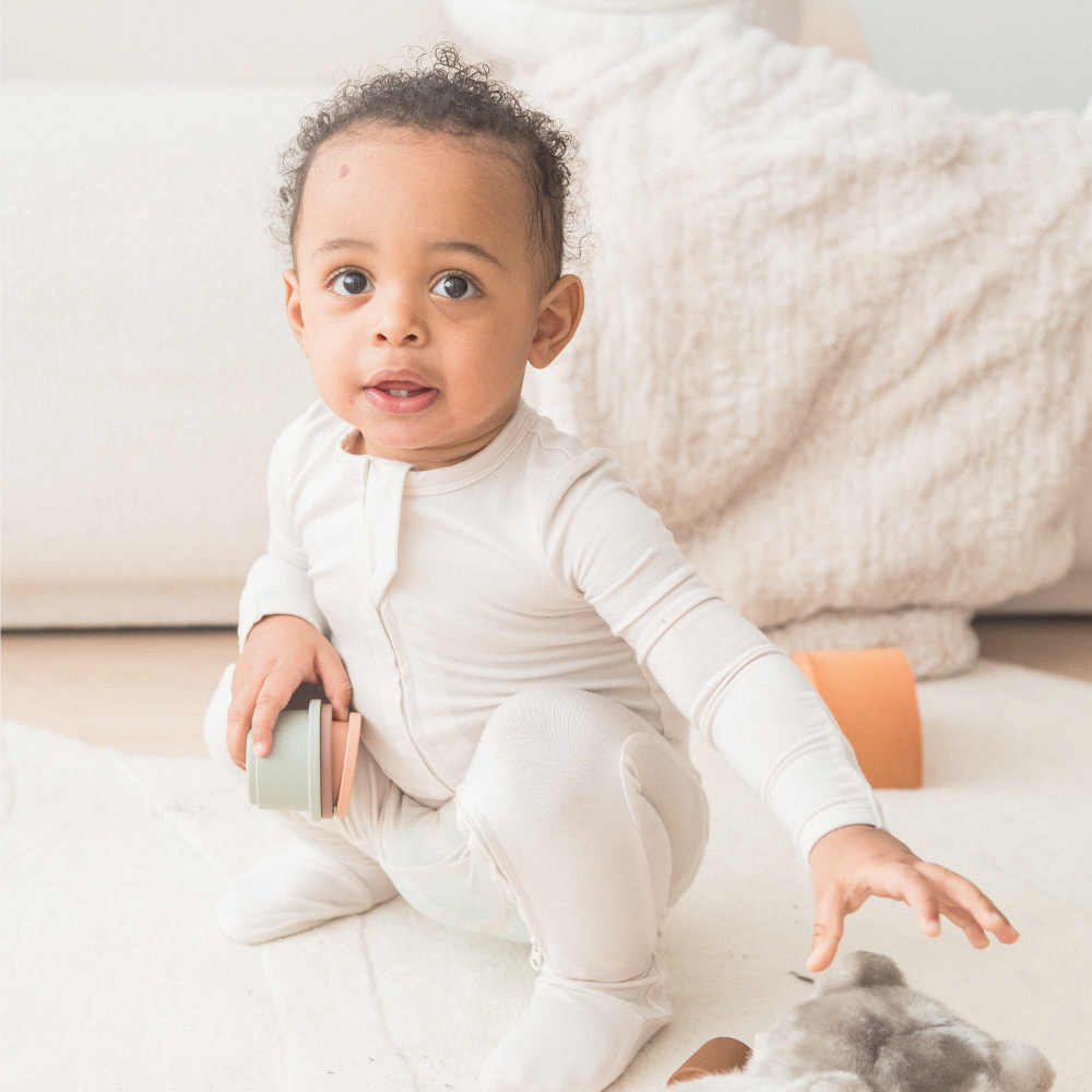 Baby in a neutral Milana Label sleeper playing with toys on the floor. 