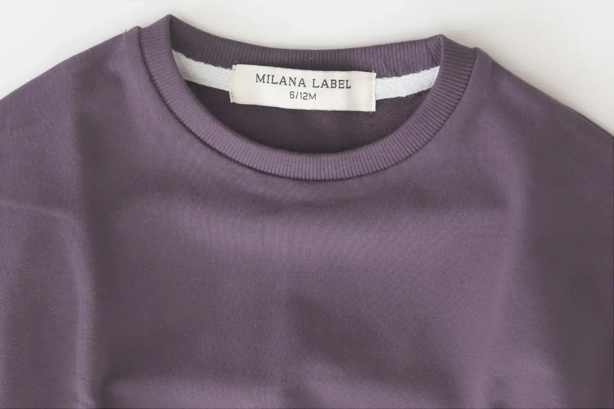 Close-up of the neckline and Milana Label size tag on a purple baby sweater.