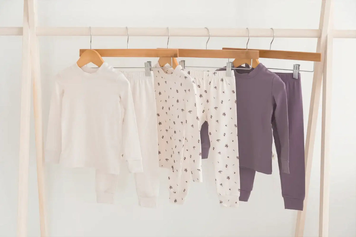 Three children's pajama sets hanging on a wooden clothing rack against a white wall. The sets are crafted from Milana Soft TENCEL fabric.
