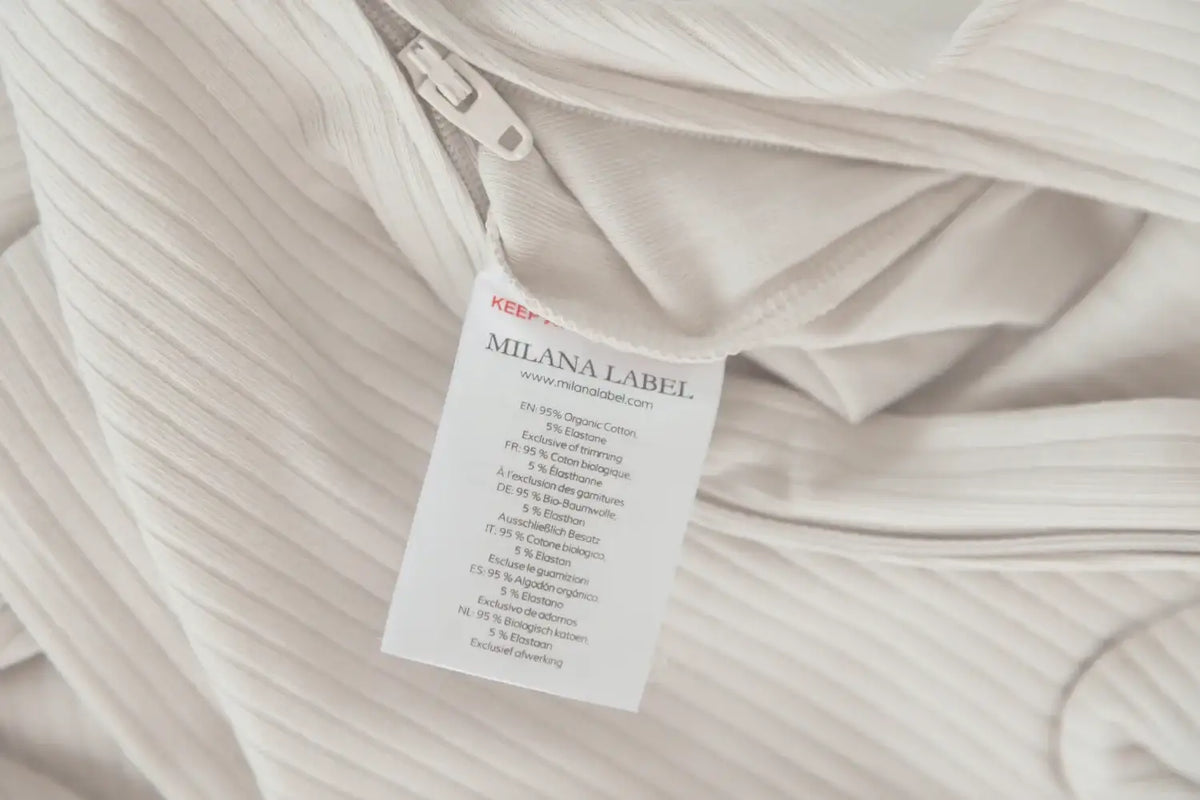 Close-up of a greige-colored ribbed fabric footie with a white sewn-in care label from Milana Label.