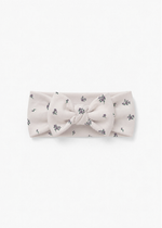 Milana Label baby bow headband in Birch Floral, warm neutral fabric with a scattered purple floral print, photographed flat against a white background.
