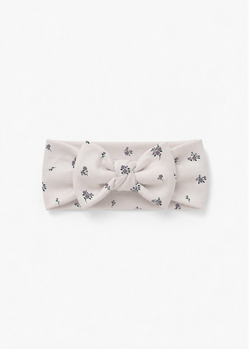 Milana Label baby bow headband in Birch Floral, warm neutral fabric with a scattered purple floral print, photographed flat against a white background.