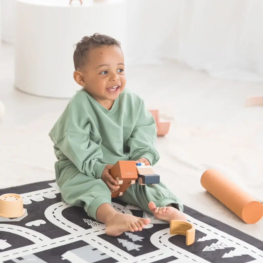 A toddler wearing a green long sleeve set playing with wooden toys on a play mat.