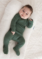 Full-length angled view of a baby resting comfortably in a white lounger, wearing the Milana Label Pine green ribbed footie pajama.