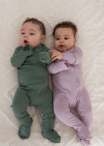 Two babies lying side-by-side on a white blanket, showcasing the full length of the Pine green and Lavender Blush organic cotton ribbed footie sleepwear.