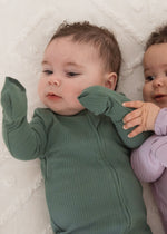Close-up view of two babies interacting on a white blanket, one wearing the Pine green ribbed sleeper and the other in the Lavender Blush sleeper.