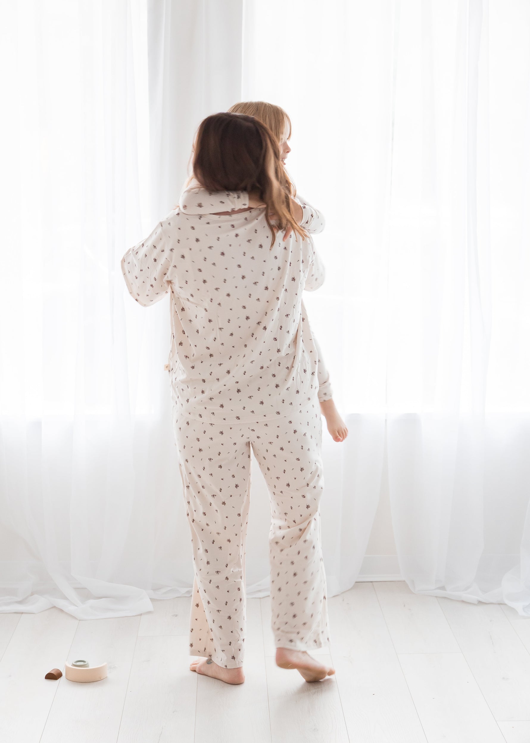 Back view of a mother holding her toddler, both wearing matching Tencel pajamas in a floral print by Milana Soft.