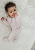 Overhead full-length view of a baby lying on a white textured blanket, wearing the Petal pink ribbed organic cotton sleeper.
