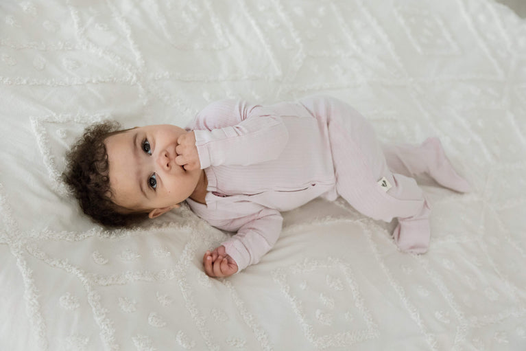 A baby wearing a pink long sleeve romper lying on a white textured blanket.