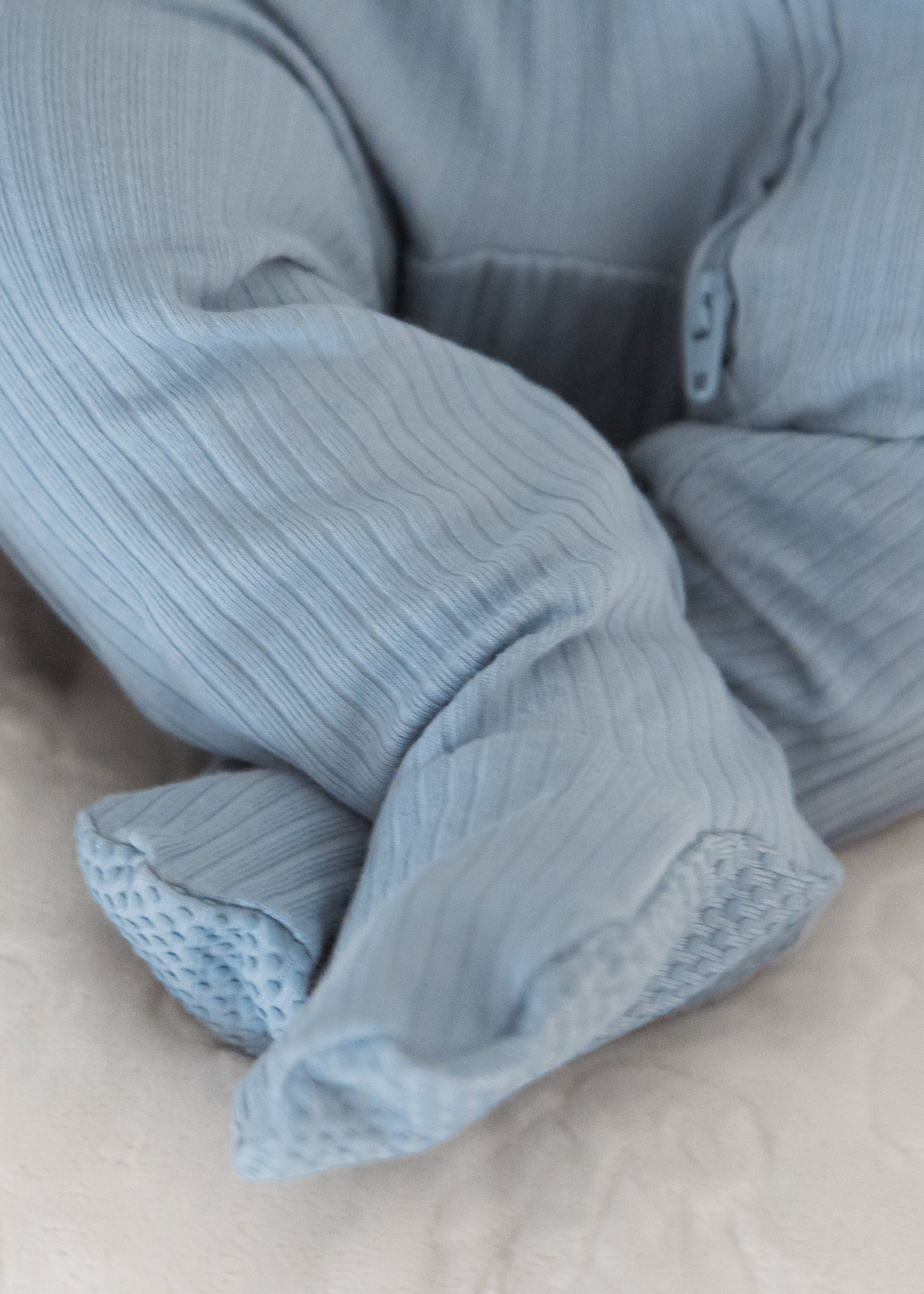 Close-up detail of a baby's feet resting in a lounger, showcasing the enclosed footies on the Soft Slate blue ribbed sleeper.