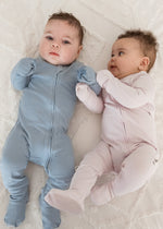 Two babies lying side-by-side on a white blanket, one wearing the Soft Slate blue ribbed sleeper and the other in the Petal pink sleeper.