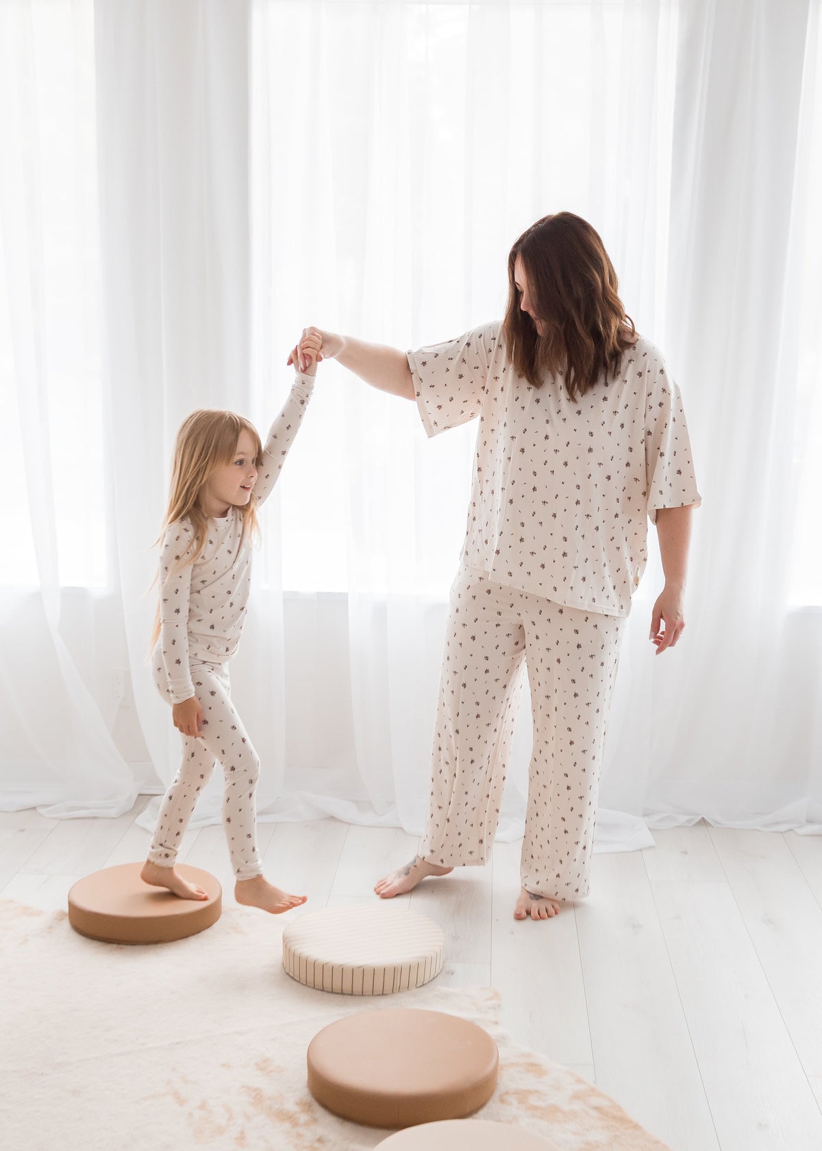 Mother and daughter holding hands and playing in matching mommy-and-me Tencel pajama sets in a birch floral print.