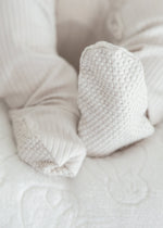 Close-up detail of the textured, built-in foot grips on the bottom of the Stone greige organic cotton baby sleeper.