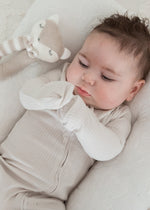 Overhead view of a baby wearing the Stone greige organic cotton sleeper with fold-over mitts, resting next to a plush teething toy in a white lounger.