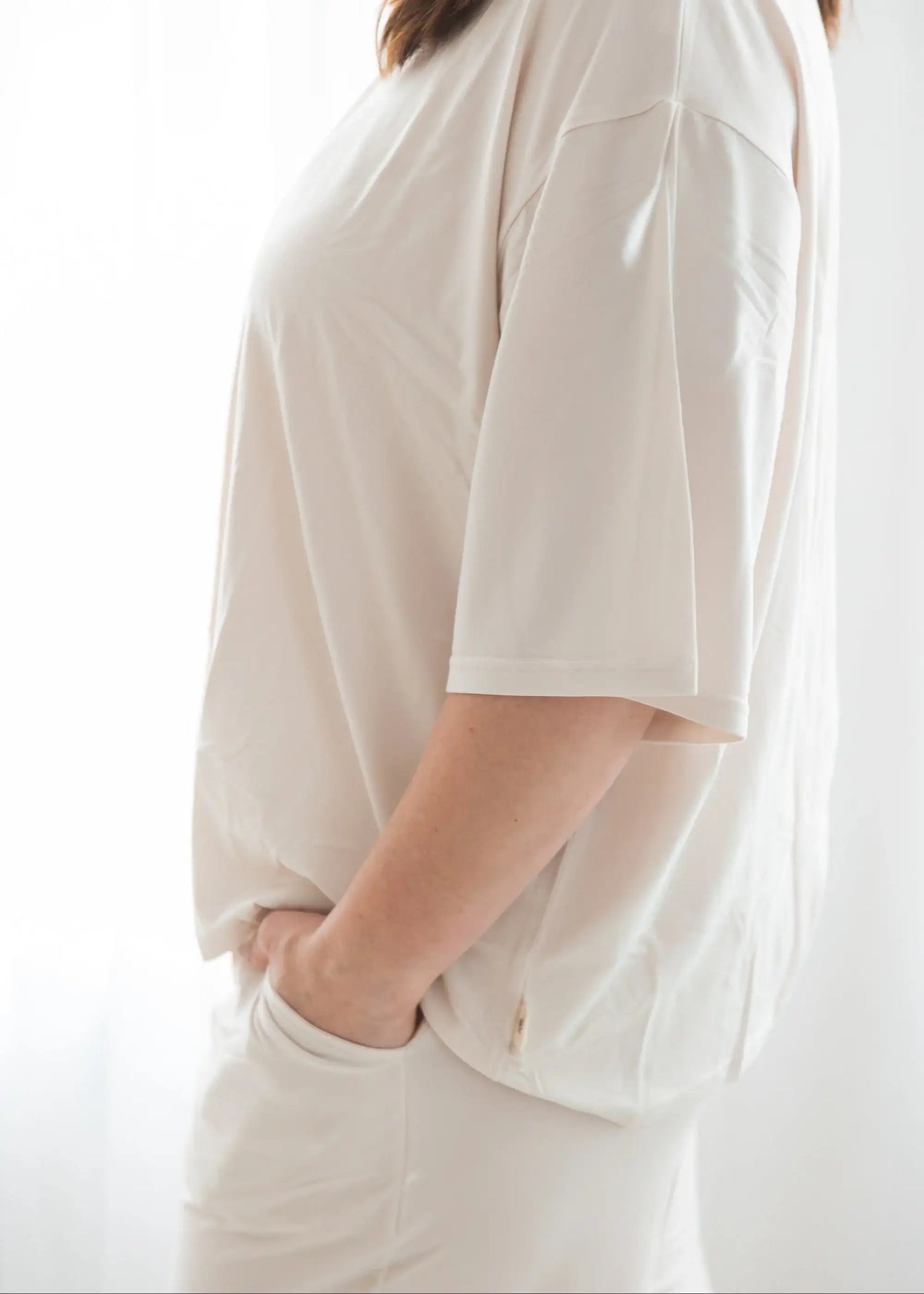 Close-up side view of a woman wearing the Milana Label women's short sleeve lounge set in Birch, showing the relaxed fit of the t-shirt and a hand resting casually in the pants pocket against a bright white background.