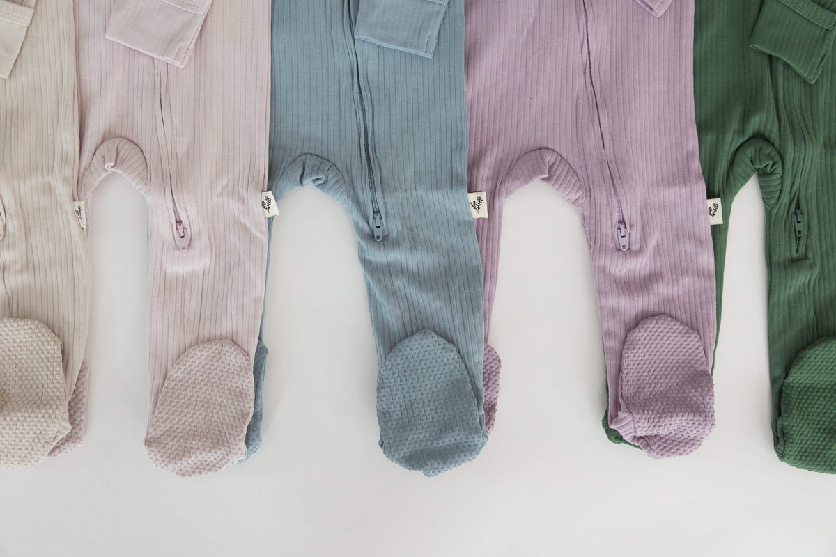 Five ribbed baby zip-up sleepers in greige, pink, blue, purple, and green.