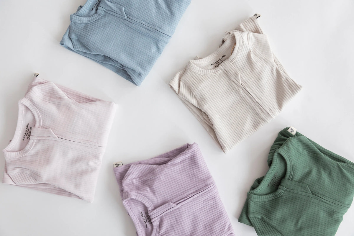 Four baby ribbed zip sleepers in blue, greige, pink, purple and green flat lay.