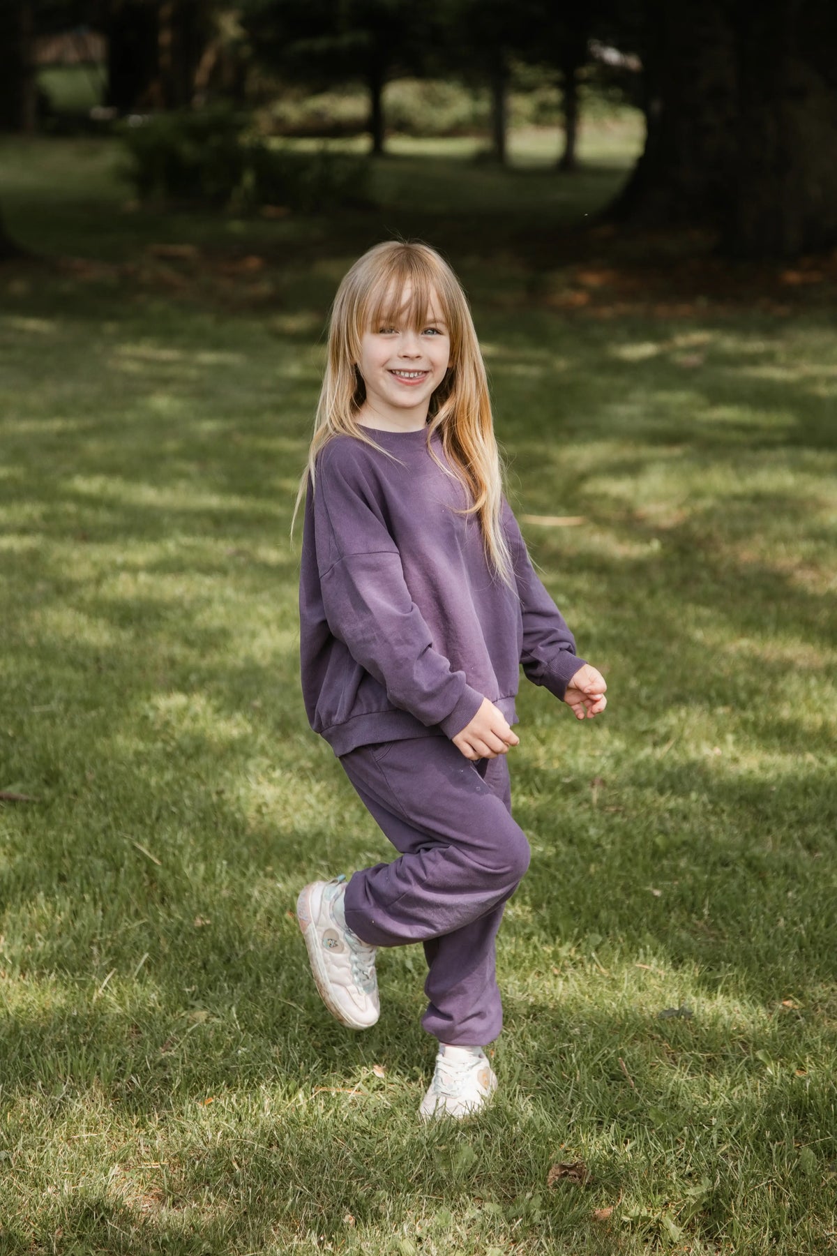 A child wearing a purple sweatshirt and matching joggers standing in a grassy field.