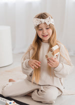 A little girl playing with a toy car while sitting on the floor in her jogger set with Milana Soft knot headband.