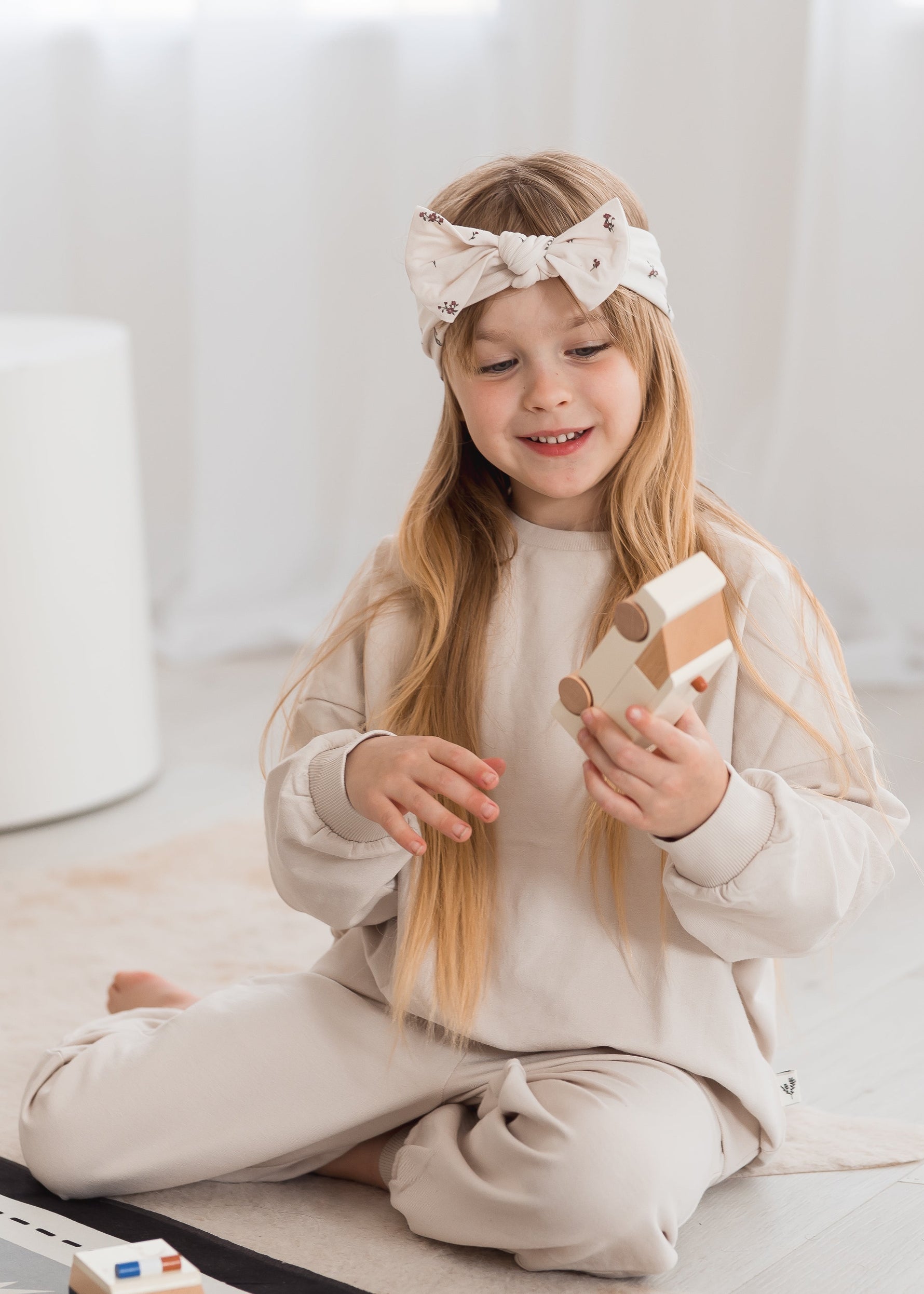 A little girl playing with a toy car while sitting on the floor in her jogger set with Milana Soft knot headband.