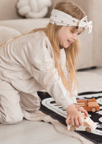 A kid playing with toy cars on a play mat while wearing a Milana Label knot headband in the colour Birch Floral.
