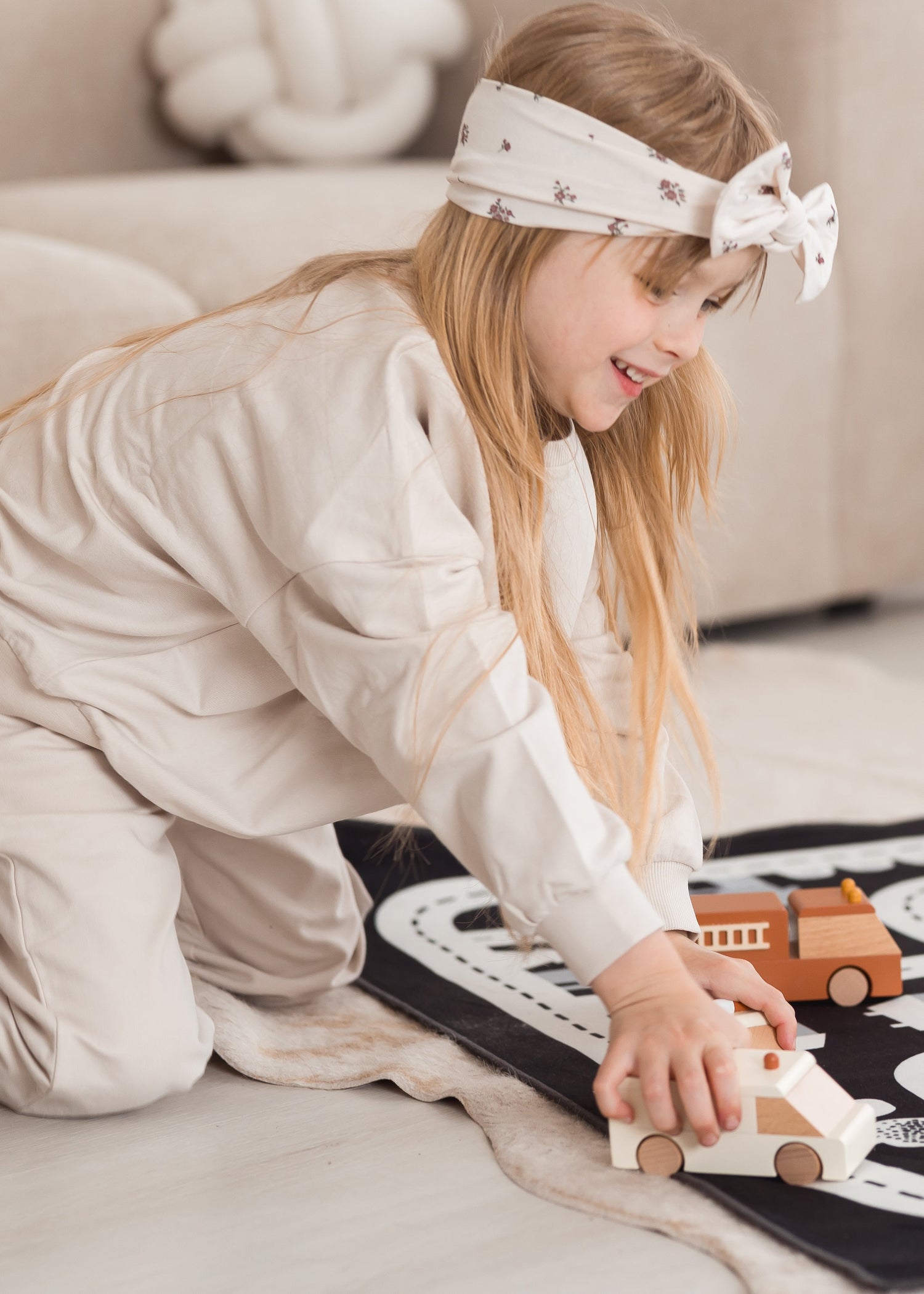 A kid playing with toy cars on a play mat while wearing a Milana Label knot headband in the colour Birch Floral.