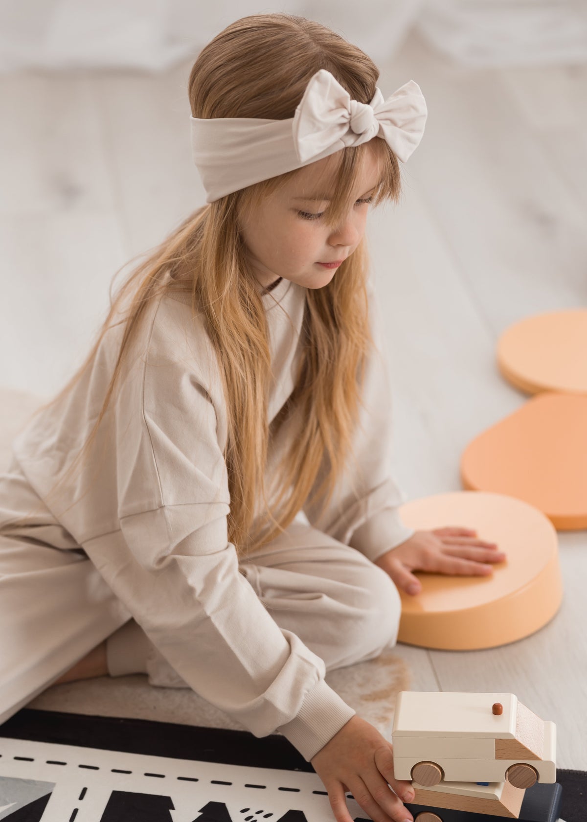 A kid playing on the floor with cars while wearing a Milana Label headband in a soft neutral colour.