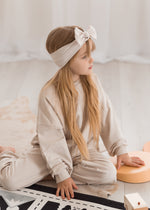 Side profile closeup of a young girl with long blonde hair wearing a neutral, certified organic cotton jogger set as she plays in a sunlit playroom.