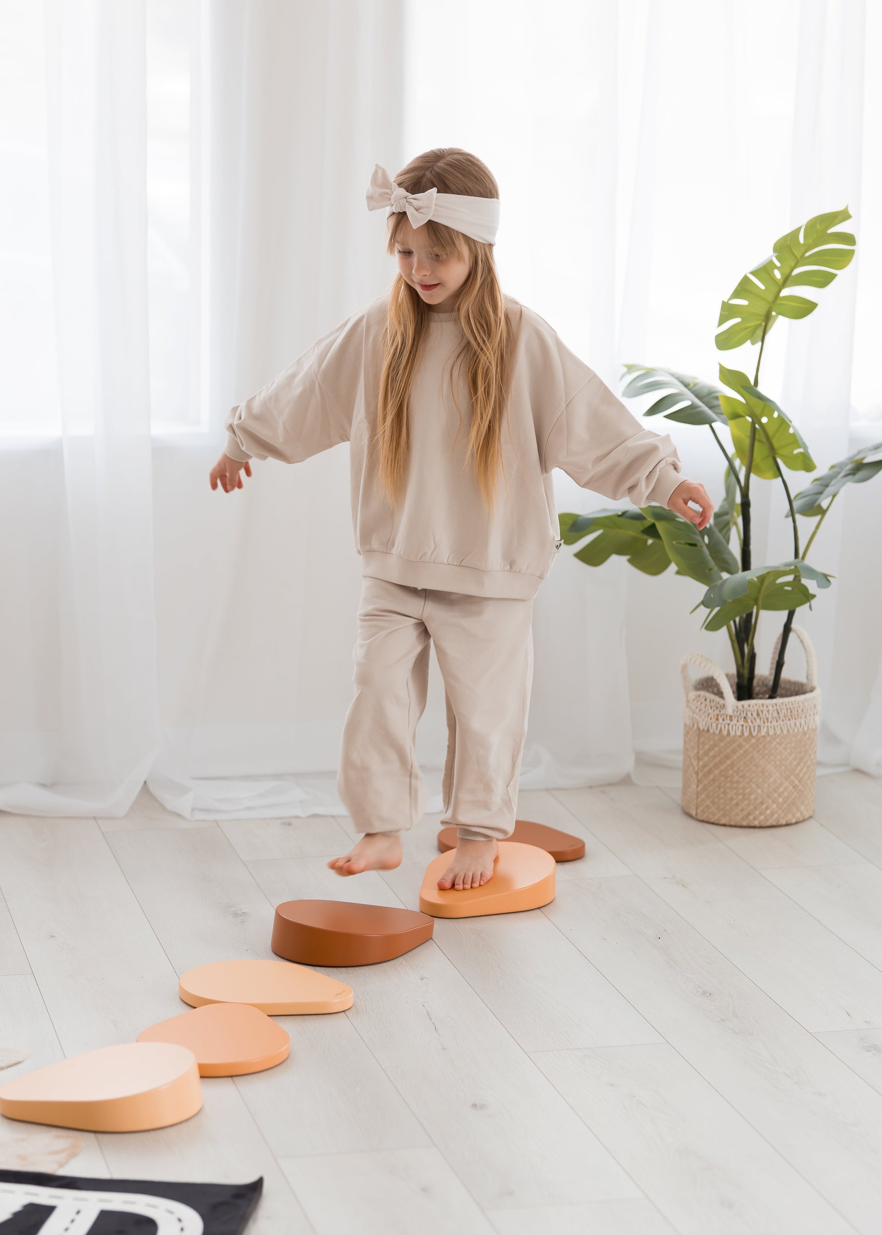 A kid playing on steppers while wearing a knot headband in the colour Birch by Milana Label.