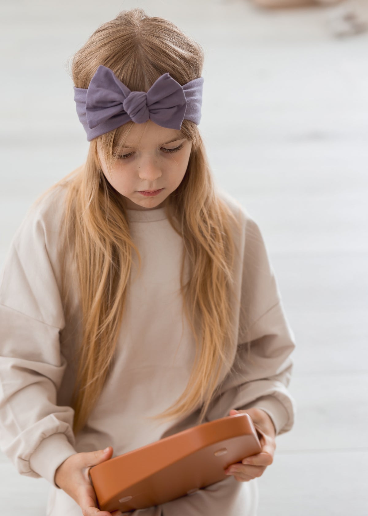 A kid playing with steppers on the floor while modelling the Milana Label knot headband in the colour Wild Mulberry.