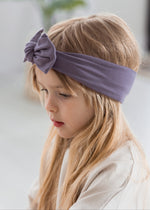 A closeup of a kid wearing the Milana Soft knot headband in the colour Wild Mulberry. A greyed neutral purple.