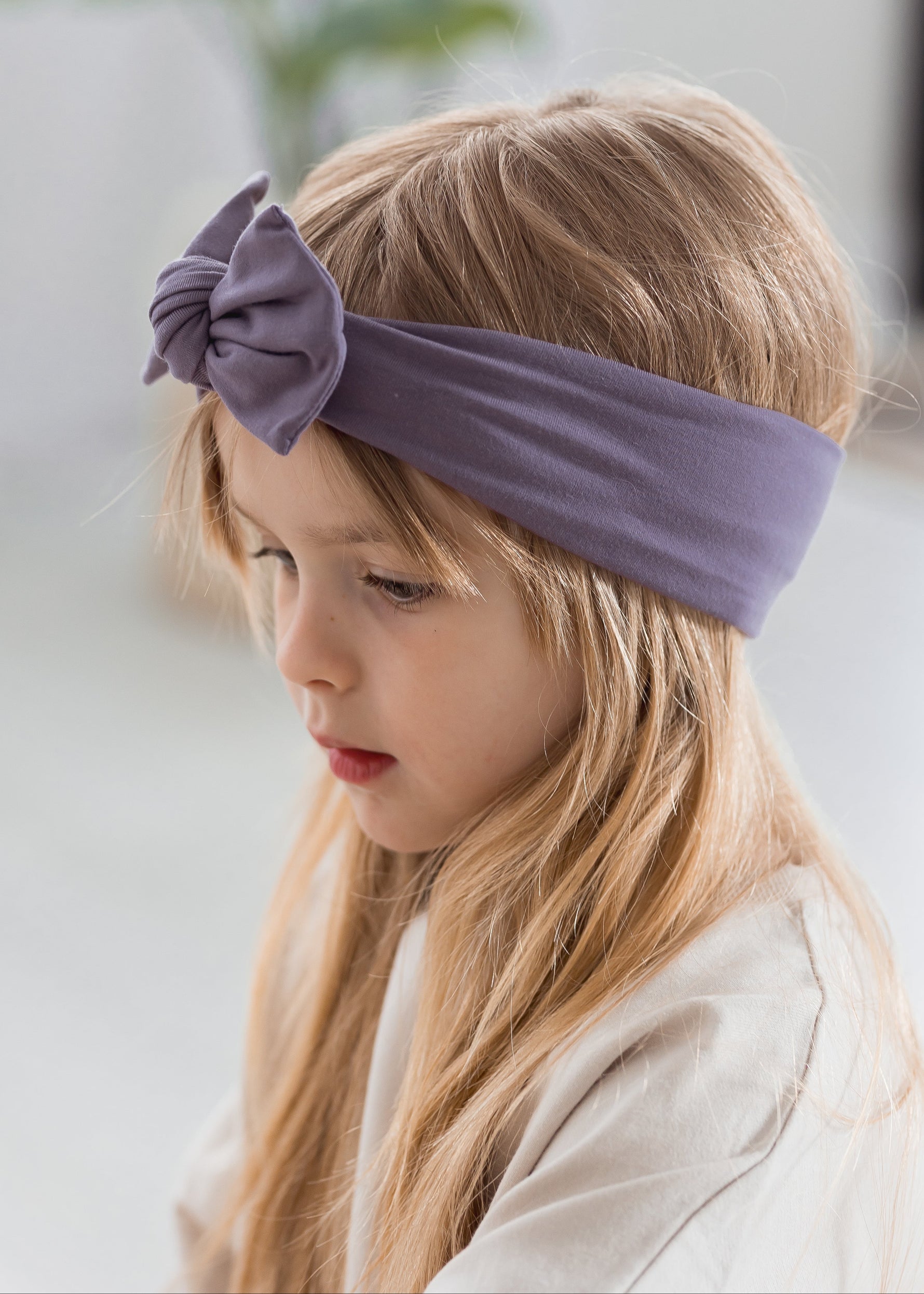 A closeup of a kid wearing the Milana Soft knot headband in the colour Wild Mulberry. A greyed neutral purple.