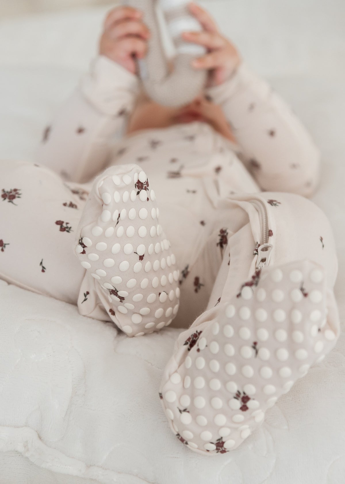 A baby lying on a white quilted mattress, wearing a floral print footed sleeper crafted from silky-soft TENCEL.