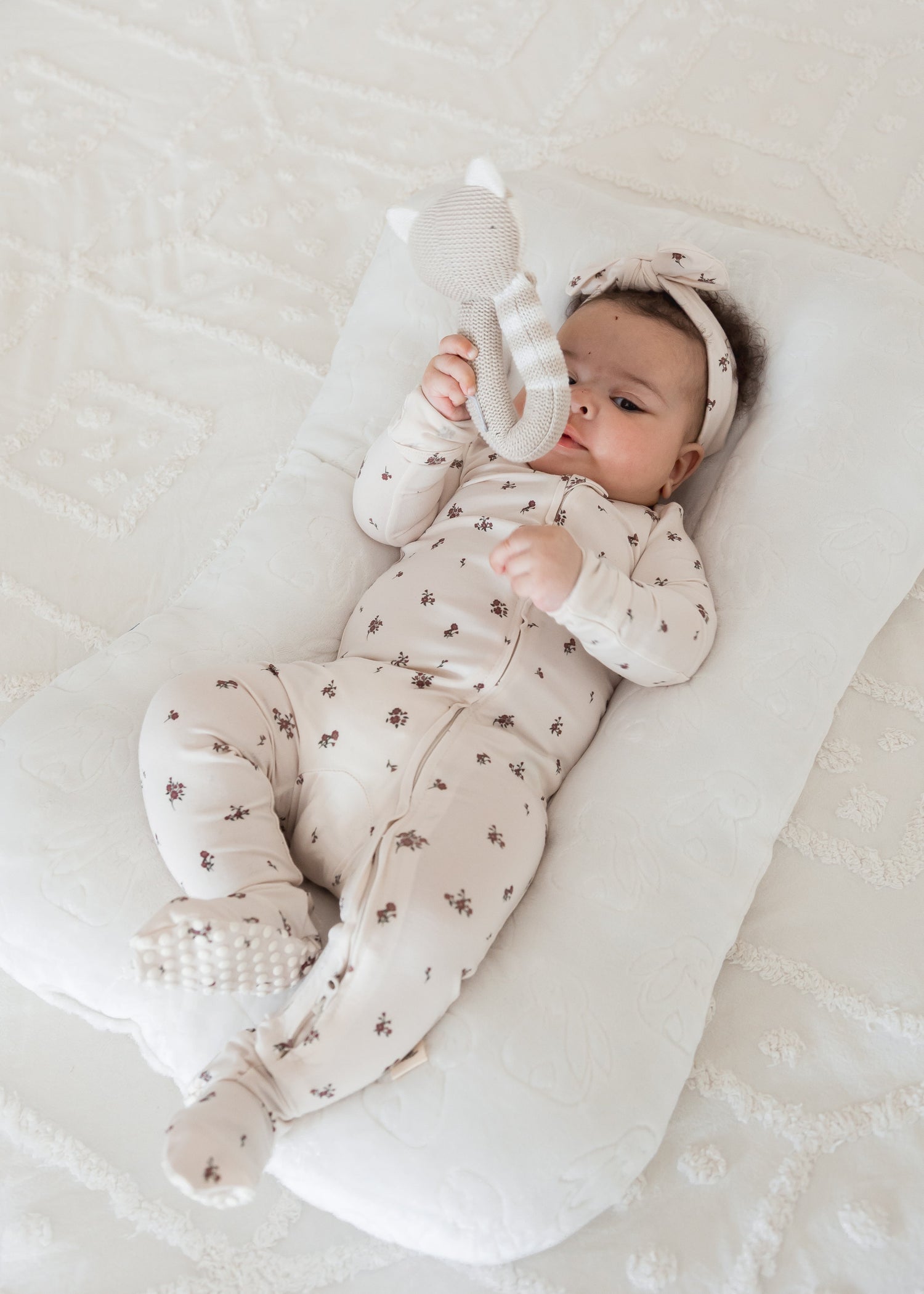 A baby playing with a toy in a Milana Label sleeper in the colour Birch Floral.