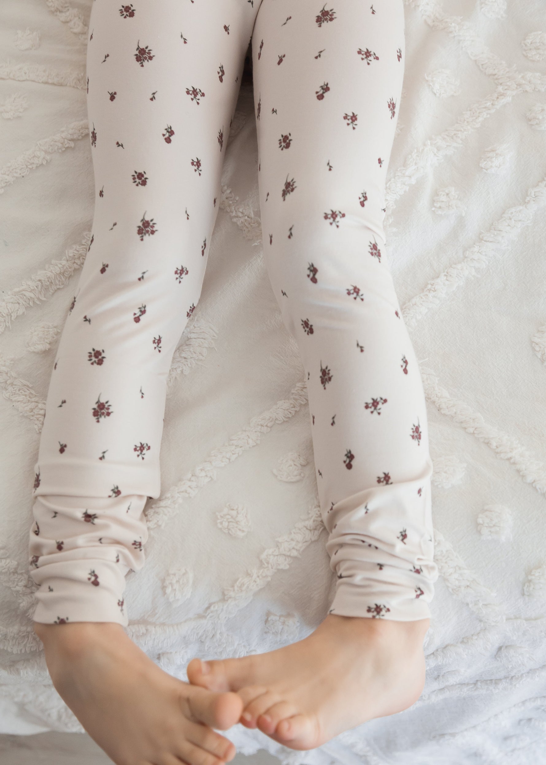 A close-up detail shot of the soft fabric and fit of a kids' Tencel long-sleeve pajama set in a birch floral pattern, showing a young girl sitting down in a bright, cozy setting.