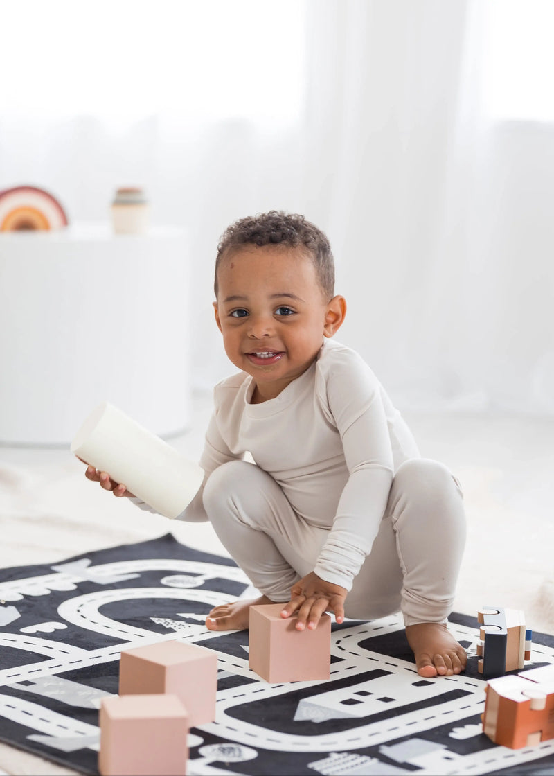Toddler smiling and playing on the floor with blocks in his neutral Milana Label PJ set.