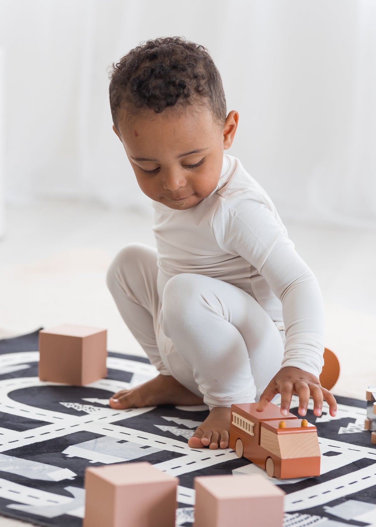 Toddler playing on a road play mat with cars in his Milana Label PJ set in the colour Birch.