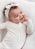 Close-up of a smiling baby wearing a Milana Soft sleeper in Birch, highlighting the premium, gentle fabric against newborn skin.