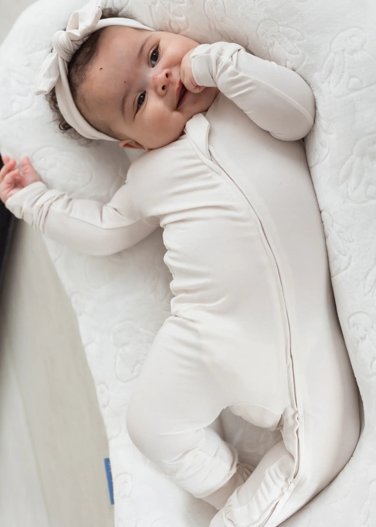 Baby laying in a lounger in her Milana Label sleeper in the colour Birch with matching headband.