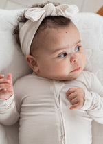 A baby lounging in a soft TENCEL sleeper and matching knot headband in a neural colour by Milana Label.