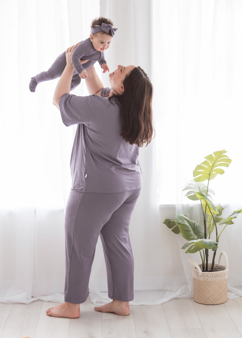 A mom and her daughter in their matching Milana Label PJ's. They are standing in front of a window while the mom holds up her daughter.
