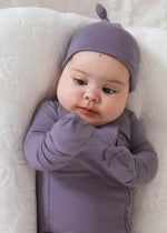A baby wearing a matching Milana Label long-sleeve bodysuit and knot bonnet, lying on a white quilted mattress.