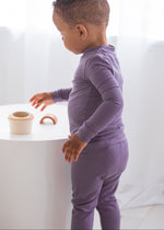 Side view of a toddler standing by a white cylindrical table, wearing a snug-fit Wild Mulberry purple TENCEL long-sleeve pajama set.