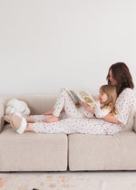 A mom and her daughter in their matching Milana PJ sets sitting on a neutral couch.