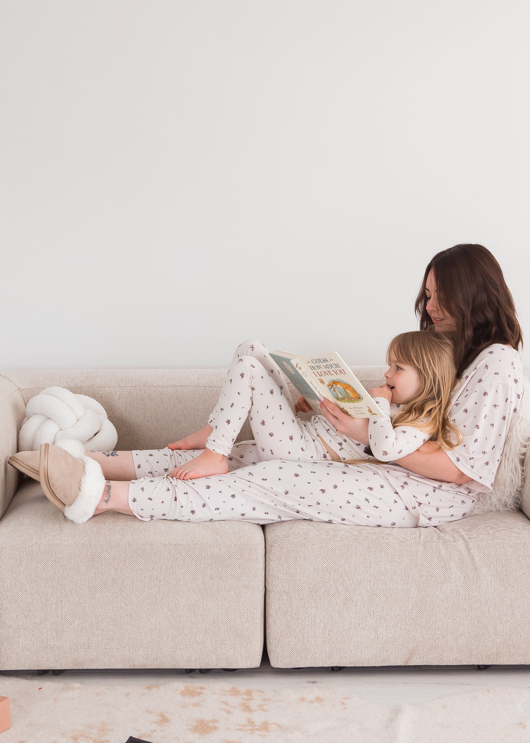 A mom and her daughter in their matching Milana PJ sets sitting on a neutral couch.