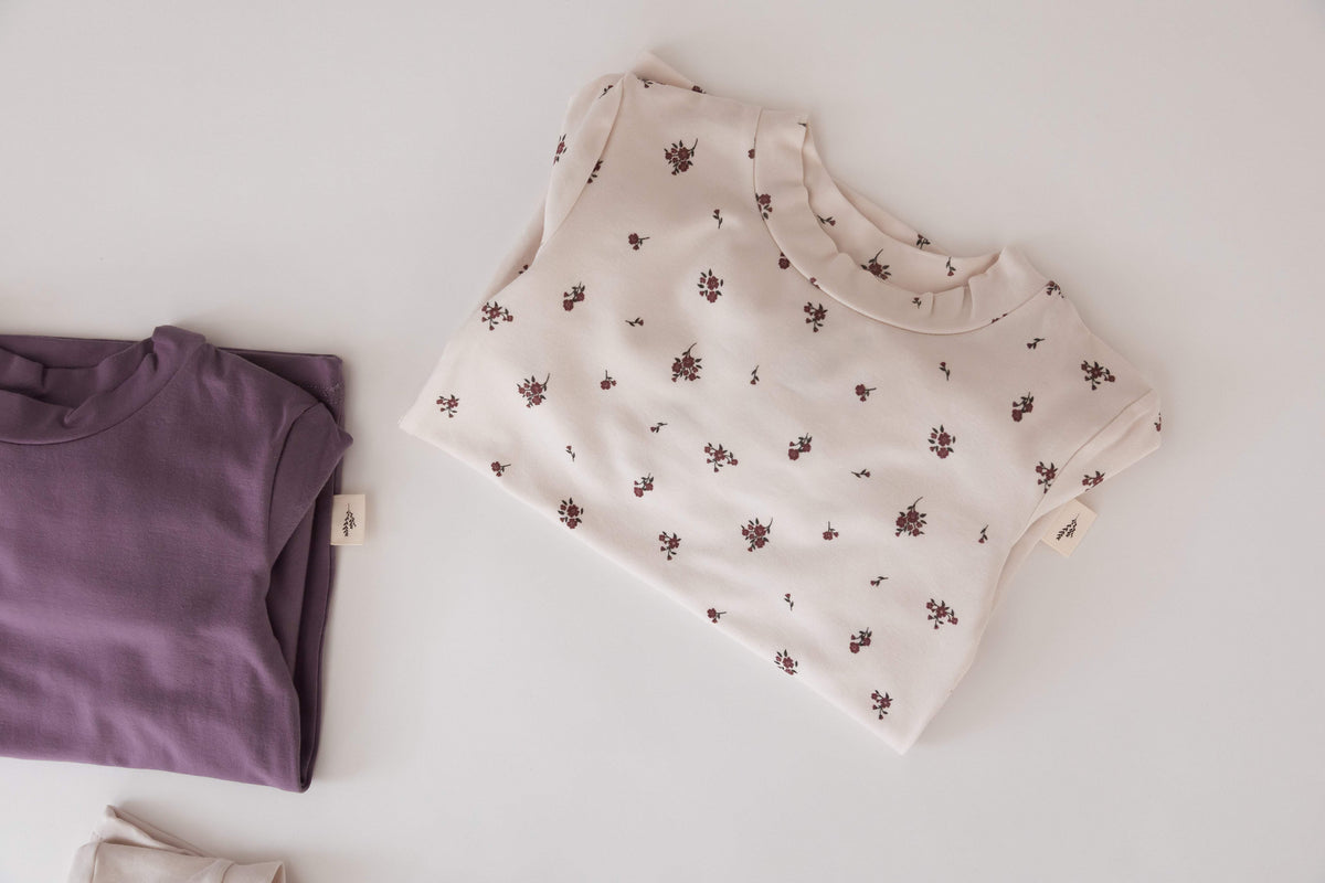 A styled flat-lay of two PJ sets on a clean white background. The shirt on the right is Birch Floral, and the shirt on the left is Wild Mulberry, both by Milana Label.