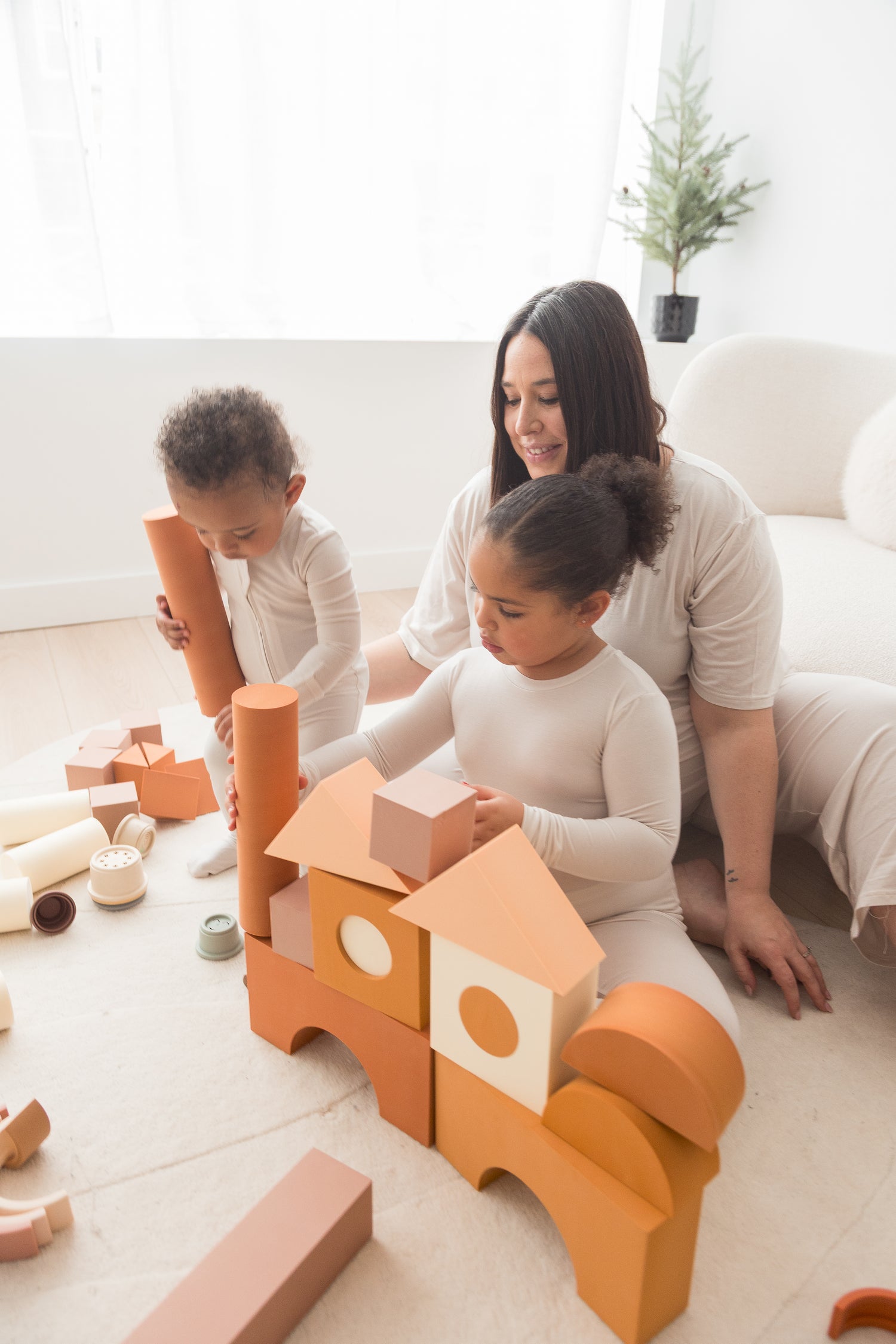 A mom and her two kids playing with blocks on the floor in their matching Milana outfits. 