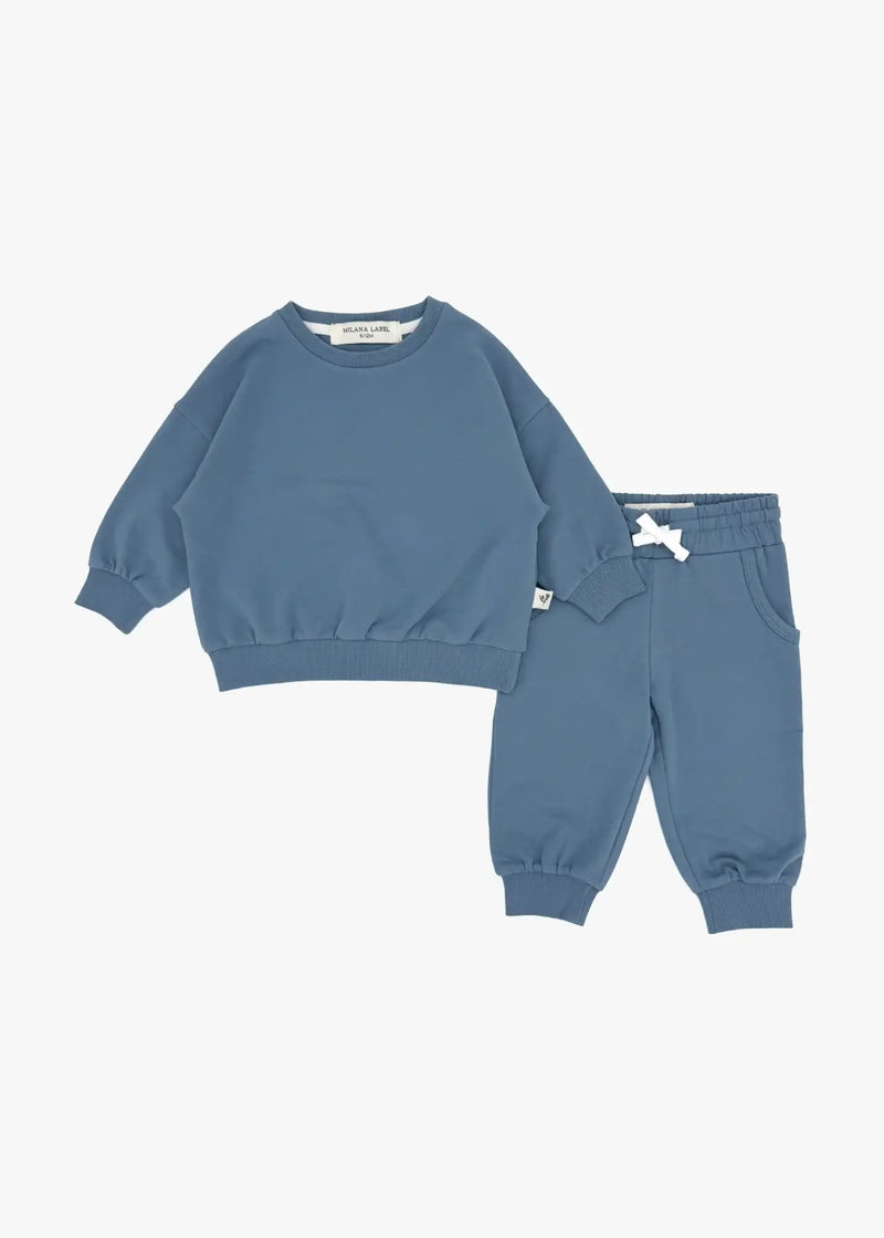 A flat lay product view of a children's two-piece organic cotton loungewear set in Nordic blue, featuring an oversized crewneck sweater and matching jogger pants with a white drawstring against a crisp white background.