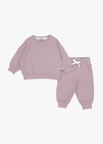 A flat lay product shot of a matching children's organic cotton jogger set in pale orchid, featuring a muted dusty pink oversized sweatshirt and matching jogger pants with a white drawstring bow against a white background.